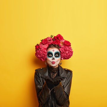 Portrait of female zombie with painted skull face, sends air kiss, expresses love, celebrates day of death, prays for family members who died comes on Mexican holiday or festival has halloween makeup