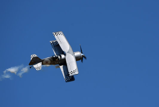  Pitts Model 12  stunt byplane  with smoke trail and blue sky.