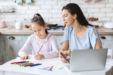Obraz premium Proud mother looking how her little daughter drawing in kitchen