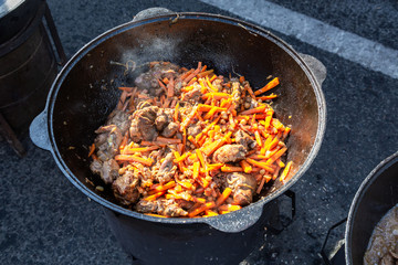 Pieces of meat cooking in a large cauldron with carrot