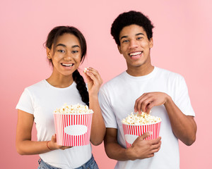 Cheerful teenagers eating popcorn on pink background