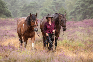 Frau wandert mit Pferden im Regen durch die Heide
