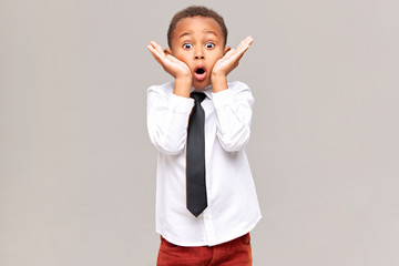 Picture of emotional funny surprised African American schoolboy in shirt and tie holding hands at...