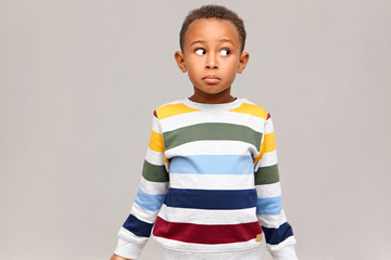 Horizontal shot of confused funny Afro American boy in striped sweater looking away with clueless facial expression, feeling guilty because he ate all sweets, pretending to be innocent. I don't know - obrazy, fototapety, plakaty