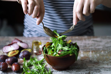 Male hands mix salad in a bowl with spoon and fork. Light salad with arugula and plums. Autumn plum salad. Healthy food. Selective focus. Macro.