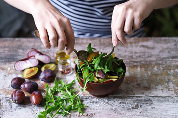 Male hands mix salad in a bowl with spoon and fork. Light salad with arugula and plums. Autumn plum salad. Healthy food. Selective focus. Macro.