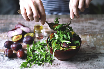 Male hands mix salad in a bowl with spoon and fork. Light salad with arugula and plums. Autumn plum salad. Healthy food. Selective focus. Macro.