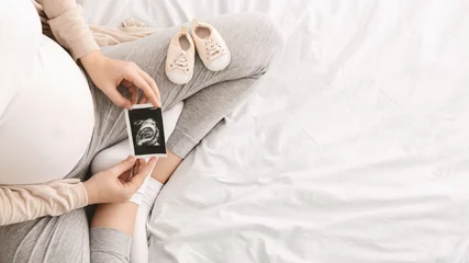Fototapeten Pregnant woman enjoying future motherhood with first ultrasound photo © Prostock-studio