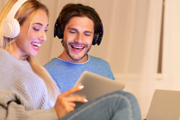 Couple In Headphones Websurfing Via Laptop And Tablet At Home