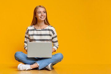 Teenage girl sitting with laptop on floor and looking aside