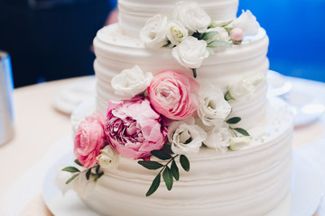 Appetizing big fresh pastry cake covered by white cream icing and decorate sweet flower serving on table. Tasty wedding event delightful dessert ready for banquet at blue light illuminate background