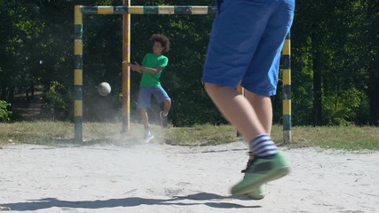 Male teenager kicking football, goalkeeper missing ball, street competition