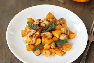dish with pumpkin. fried chicken fillet and pumpkin cubes with sage (chips from sage). a dish on the table on a sunny day. autumn dish with pumpkin.