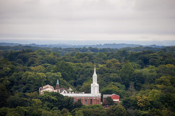 White spire on brick building rises above sea of green trees
