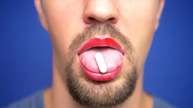 close-up. A bearded man with painted lips puts a white pill on his tongue.