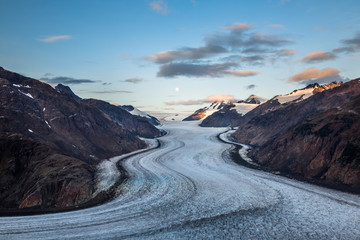 Moon setting as the sunrise lights up light clouds over the Salmon Glacier on the border between...