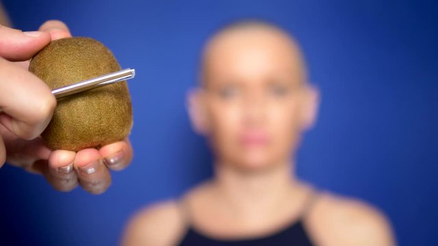 Attractive bald woman shaves a kiwi with a dangerous razor. concept of humor, adventures of strange people.