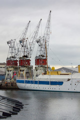Norwegian Ship with Country's Flag Moored in the Port of Oslo in the Aker Brygge District with three Cranes in the Background