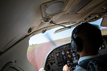 Pilot in a small airplane cockpit landing on a rural dirt airstrip