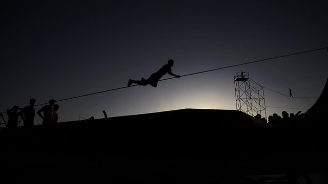 backlight Young man  balanced on slackline, on the beach, during sunset