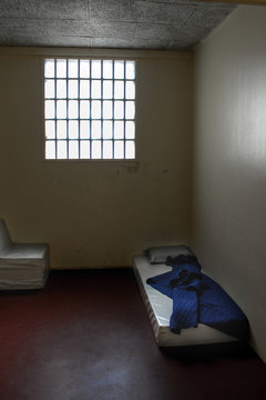 Very basic prison cell with empty mattress and blue blanket