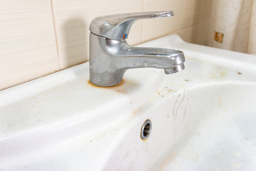 Old dirty washbasin with rust stains, limescale and soap stains in the bathroom with a faucet, water tap