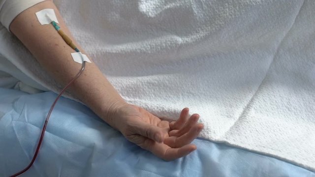 Terminally ill patients hand convulsing, dropper in arm, person suffering pain