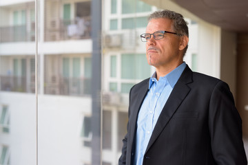 Fototapeta premium Mature Hispanic businessman thinking by the glass window of office building