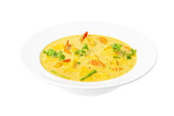 Closeup plate of thai yellow curry soup with coconut milk, shrimps, pineapple, carrot and green beans isolated at white background.