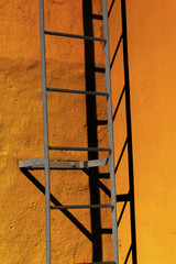 Metal ladder casting shadow in corner of concrete wall