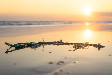 Naklejka premium A dirty beach full of pollution and plastic nets during sunset