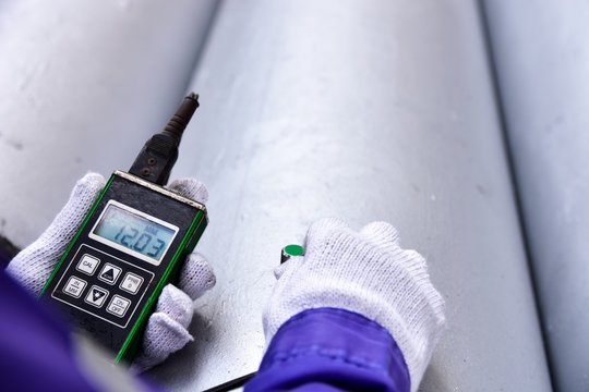 Inspector measuring thickness the pipe with UTM (Ultrasonic thickness measurement).  Selective focus on the display.