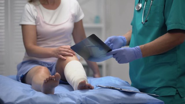 Surgeon informing knee bone x-ray result to female patient in elastic leg wrap