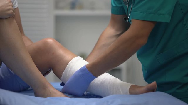 Professional surgeon applying gypsum on female patient leg, trauma, healthcare