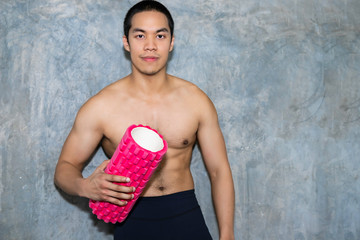 Athletic Asian man using a foam roller after a workout.