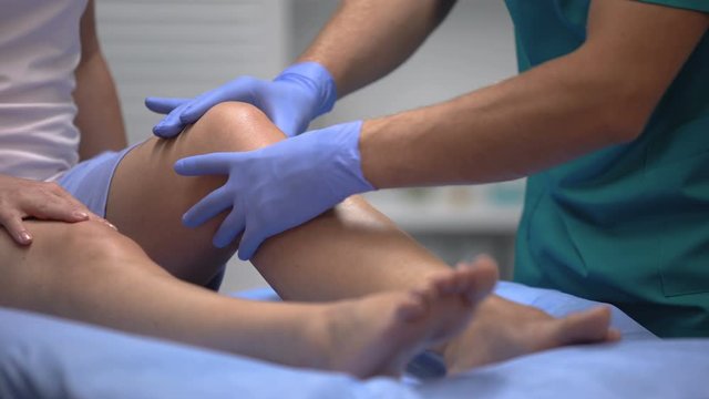 Doctor in gloves examining painful knee of female patient leg trauma, healthcare