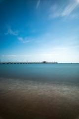 Long exposure of a beach overlooking a pier stretching out into the sea on a sunny day at Shorncliffe, Queensland, Australia.