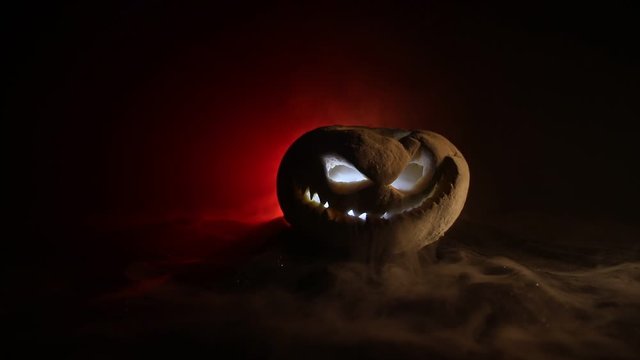 Horror concept. Scary Halloween pumpkin with carved eyes and a smile with burning candles and an ax on a dark toned background. Empty space. Selective focus