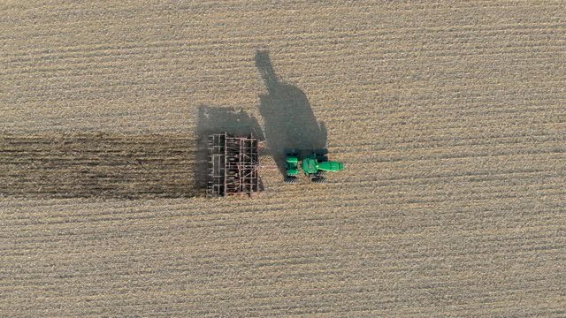 Beautiful Tracking Top-Down Aerial Drone Shot of a Green Tractor Plowing a Field with a Shadow on a Warm Summer Day.