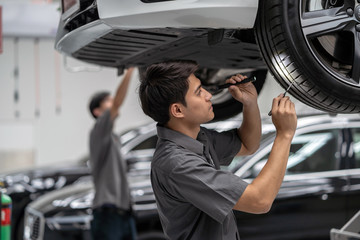 Asian mechanic Checking and torch tire in maintainance service center which is a part of showroom,...
