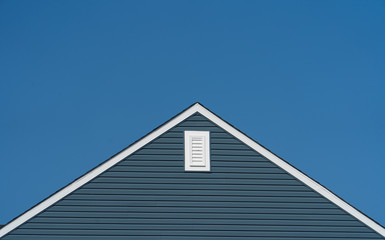 Gable with blue horizontal vinyl lap siding,  classic vertical surface mount PVC gable vent  on a pitched roof attic at an American single family home neighborhood USA © tamas