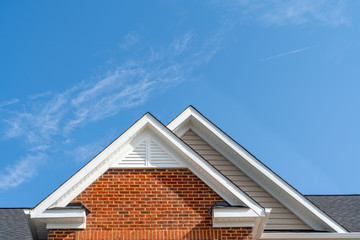 Double gable with beige horizontal vinyl lap and red brick facade siding,   with triangle shape white attic vent  on a pitched roof attic at an American single family home neighborhood USA