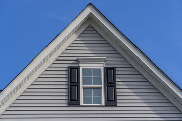 Gable with horizontal vinyl lap siding, double hung window with white frame, double vinyl shutters yellow shingle facade on a pitched roof attic at an American single family home neighborhood USA