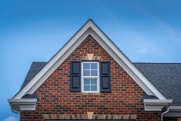Gable with red brick facade siding, double hung window with white frame, vinyl shutters on a...