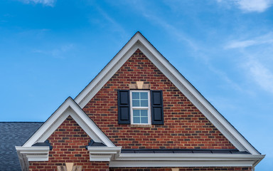 Double gable with red brick facade siding, double hung window with white frame, vinyl shutters on a pitched roof attic at a luxury American single family home neighborhood USA