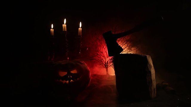 Horror concept. Scary Halloween pumpkin with carved eyes and a smile with burning candles and an ax on a dark toned background. Empty space. Selective focus