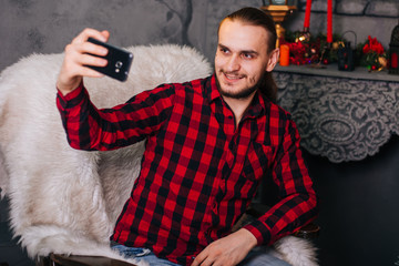 A young guy takes a selfie on a smartphone. A man sitting in a chair communicating using a video call.