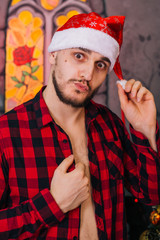 Sexy Guy in a red Santa Claus hat is holding a wince. Bearded man with an emotional face. Christmas decor