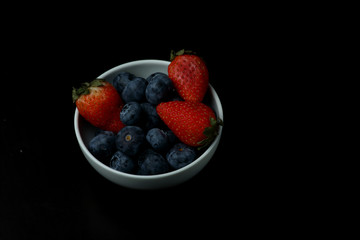 a bowl of strawberry and blueberry isolated on black background