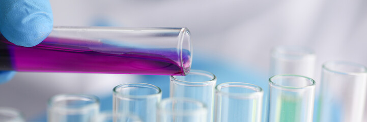 A male chemist holds test tube of glass in his hand overflows a liquid solution of potassium permanganate conducts an analysis reaction takes various versions of reagents using chemical manufacturing.